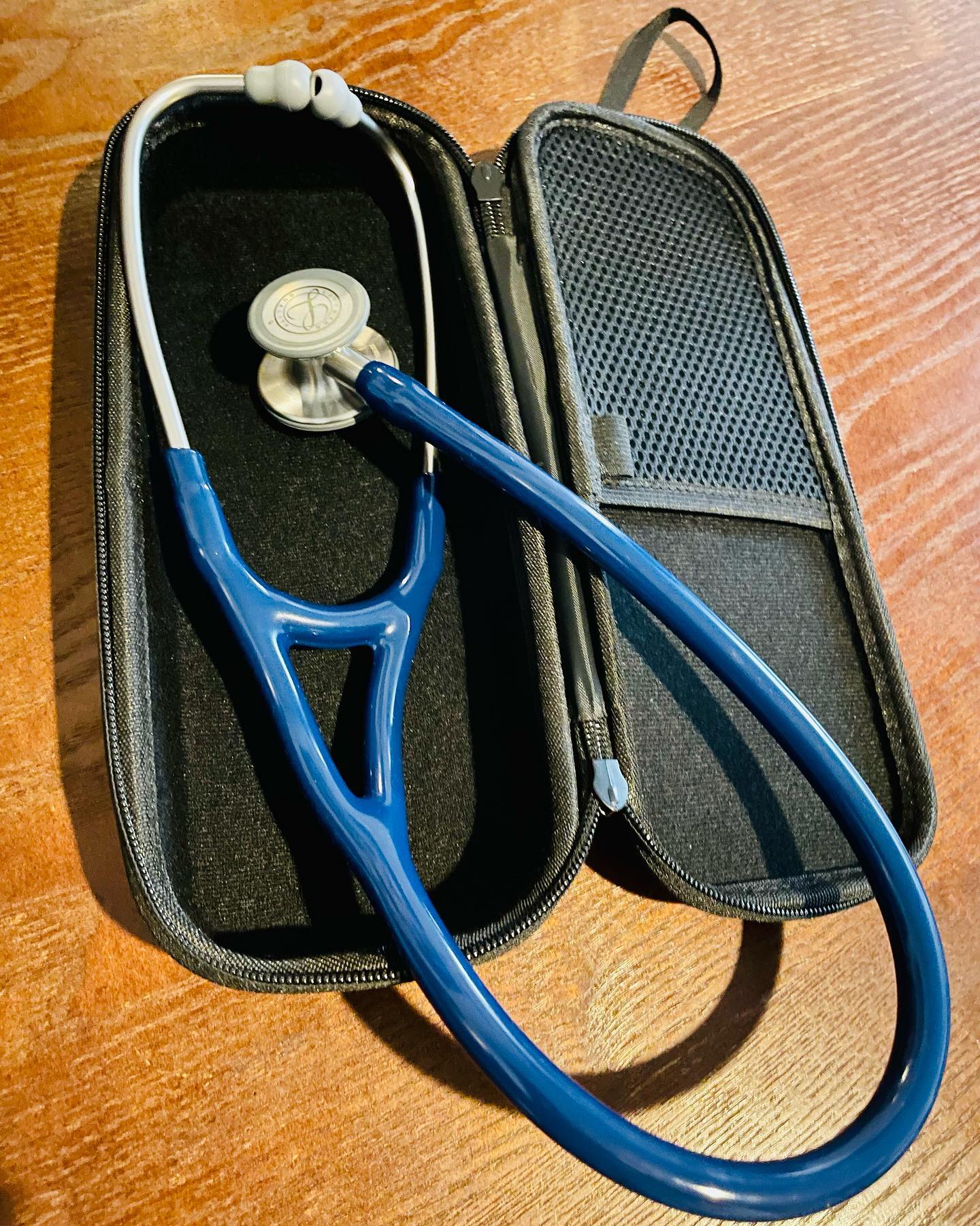 A navy stethoscope resting in its open carrying case on a wooden surface.
